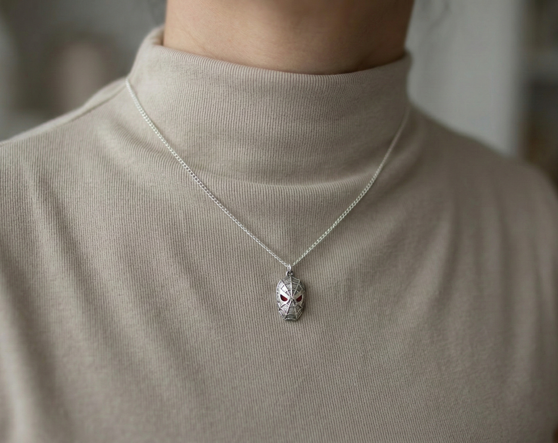 Woman modeling a chunky silver spider mask necklace over a beige turtleneck