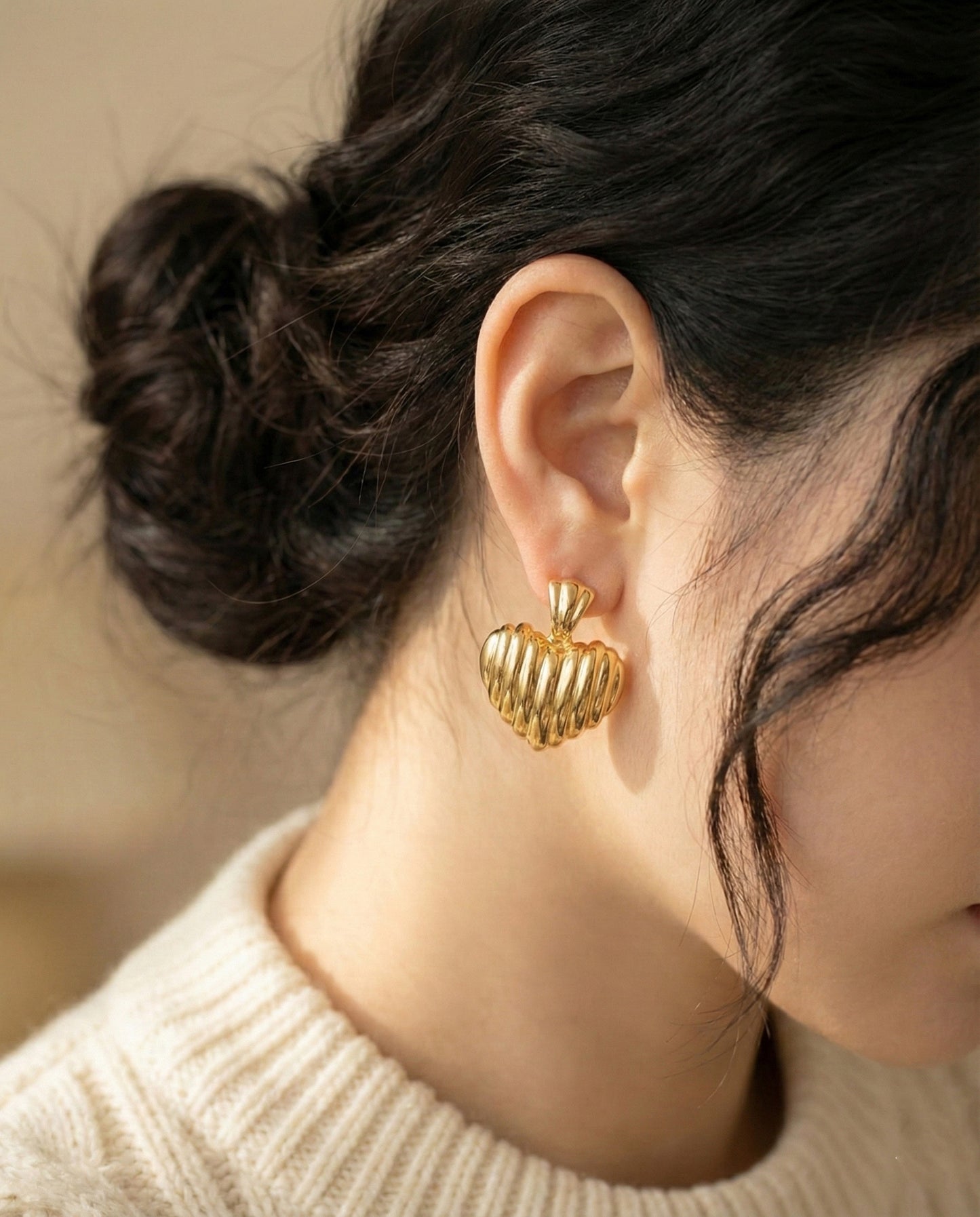 Woman in cream sweater wearing gold chunky heart earrings profile view