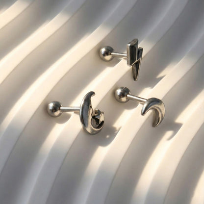 Three celestial barbell studs on white box - moon face star, crescent, lightning bolt