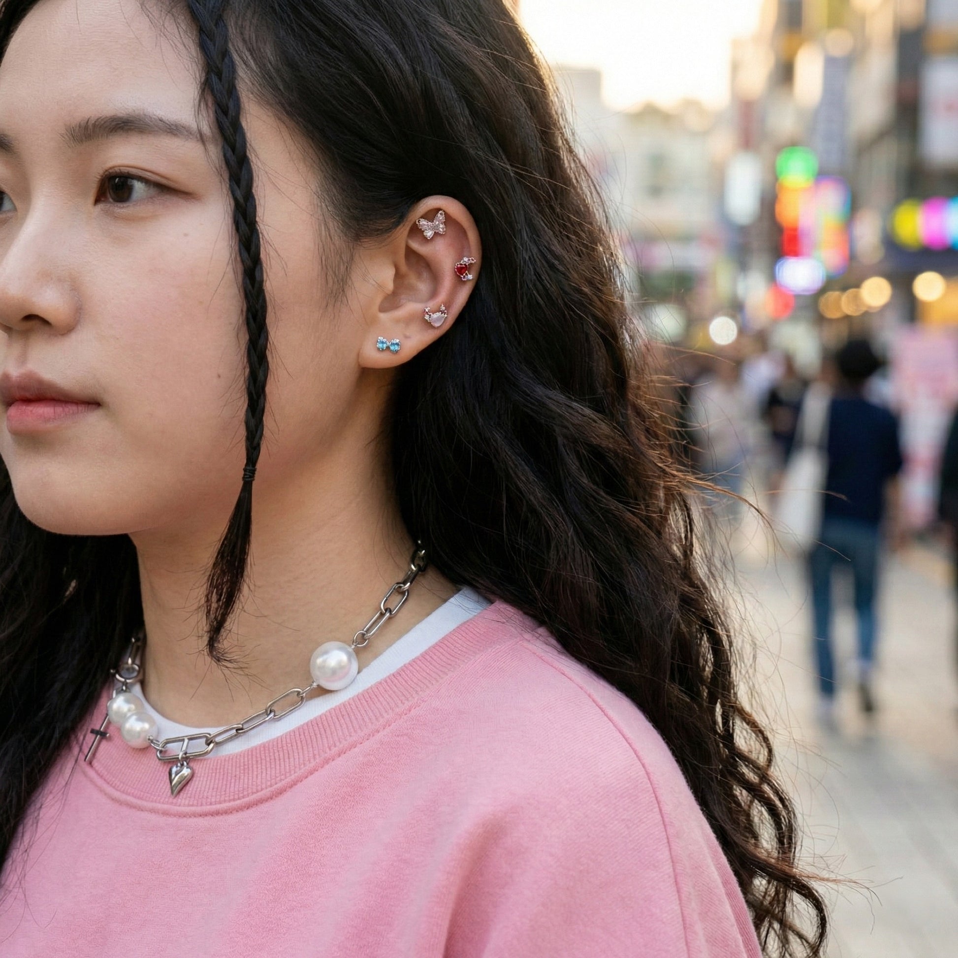 Woman wearing Y2K aesthetic outfit with pink sweater, pearl chain necklace, and layered ear piercings including moon heart stud