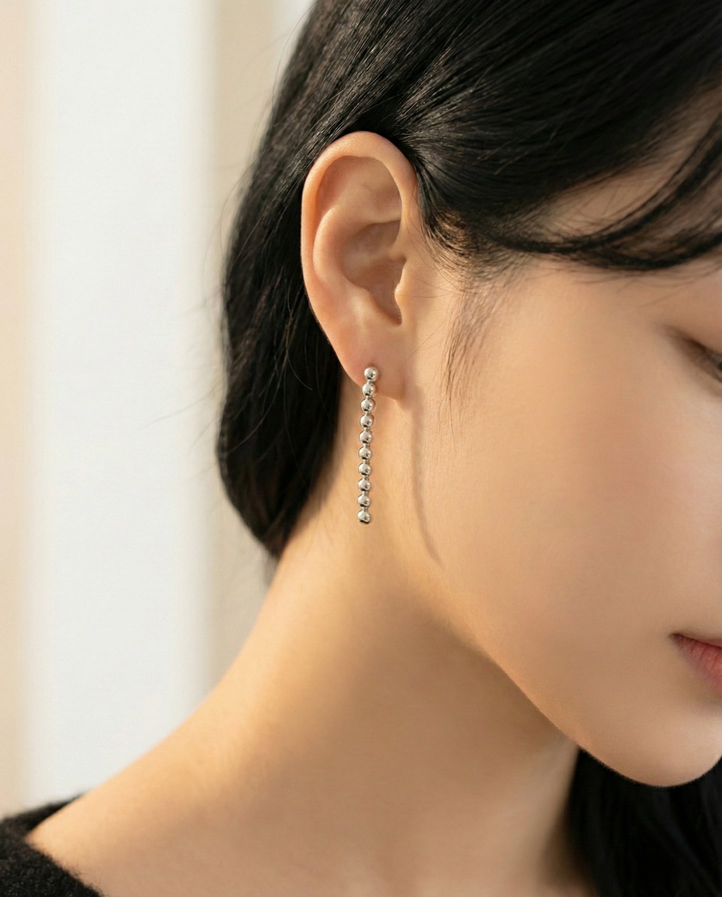 Minimal styling of woman wearing silver ball drop earrings with black outfit"