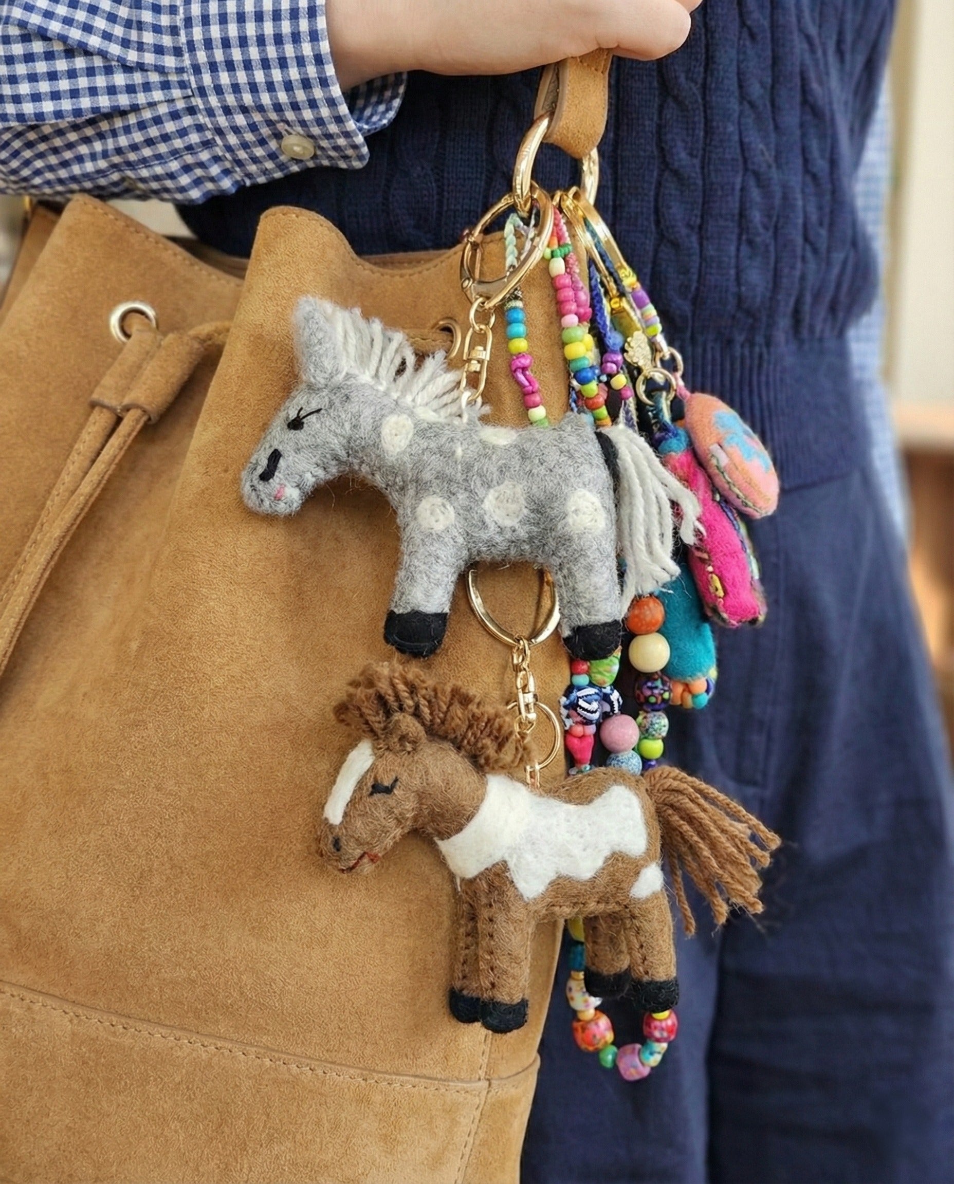 Two felt horse keychains in grey and brown with beaded straps on camel suede bucket bag