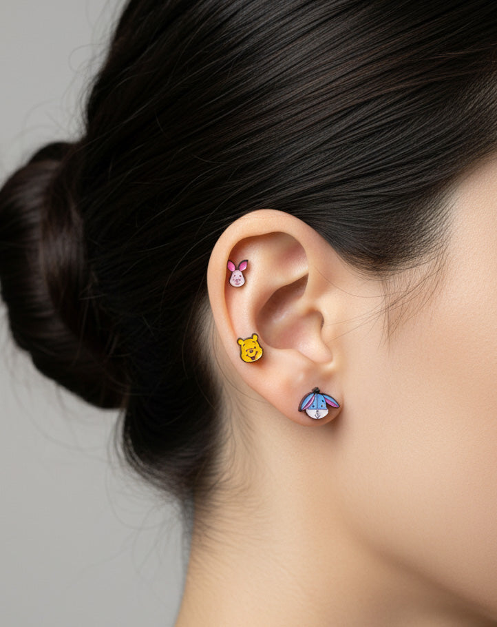 Three character barbell piercings (Piglet, Pooh, Eeyore) worn together on one ear in a cute, layered style.