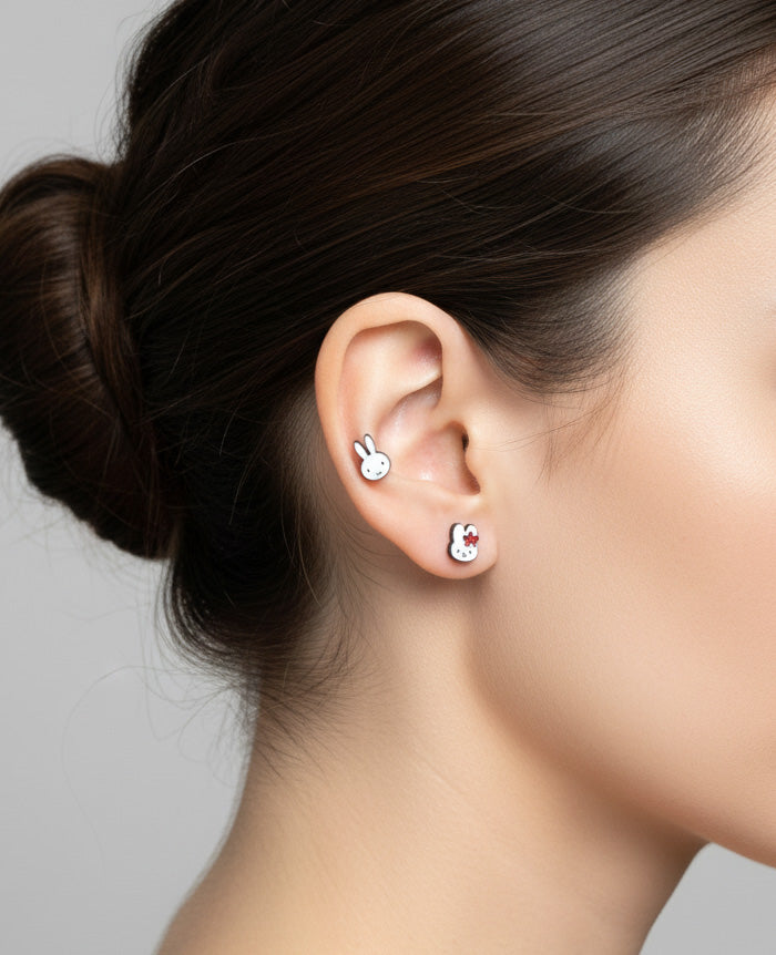 Model ear with two Miffy character earrings: one in the upper cartilage with a red flower and the other on the earlobe as a plain Miffy face; hair styled in a bun for clear focus.