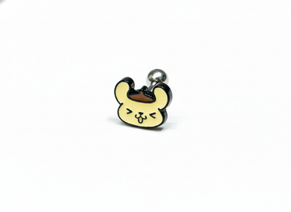 A close-up of a barbell piercing with a smiling Pompompurin face design, featuring a beret and playful expression on a white background.
