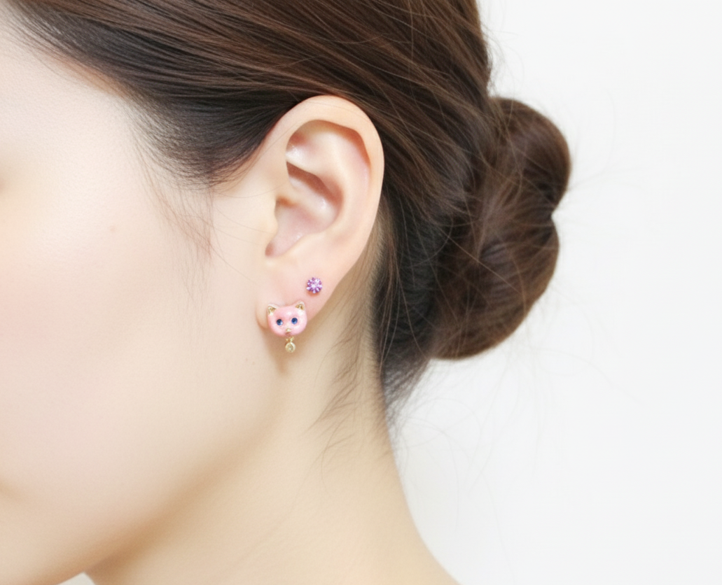 Model wearing pink enamel cat stud earrings with a tiny pearl drop, styled with an additional small lavender stud above