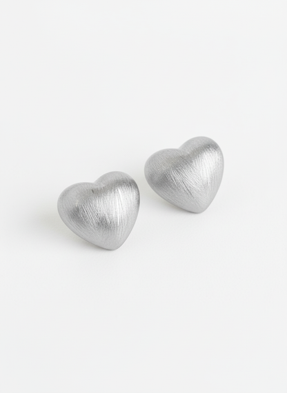 silver brushed-metal heart stud earrings on a bright white background, highlighting the soft metallic texture