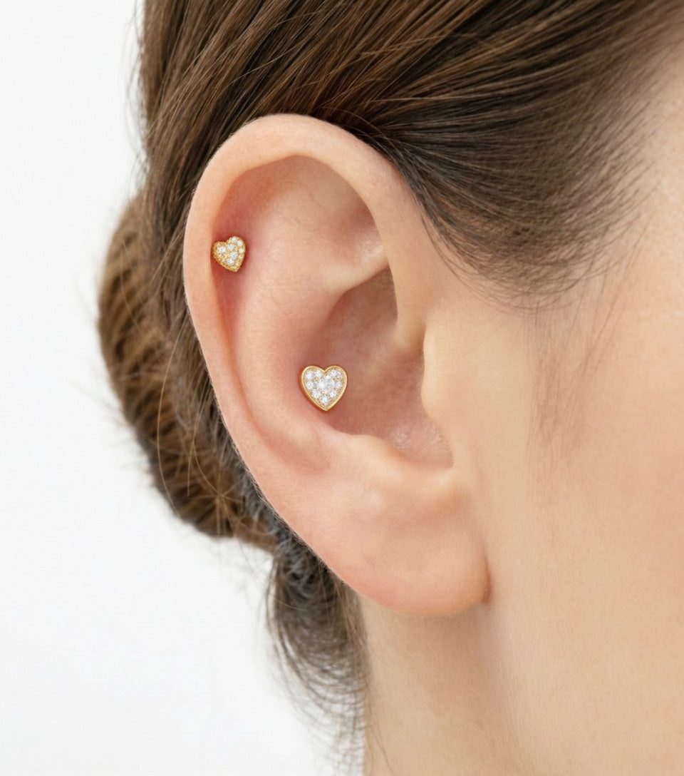 Close-up of ear wearing two gold pavé heart barbell earrings in stacked helix and lobe positions.