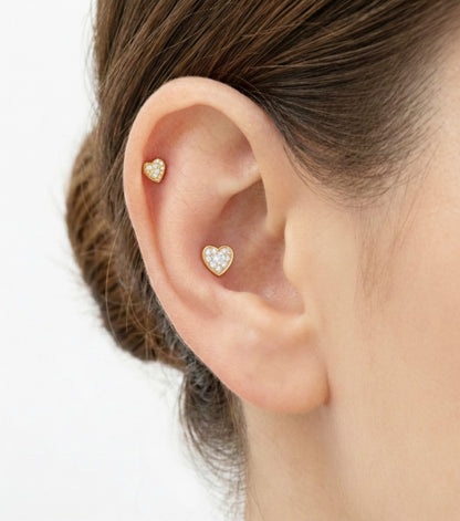 Close-up of ear wearing two gold pavé heart barbell earrings in stacked helix and lobe positions.