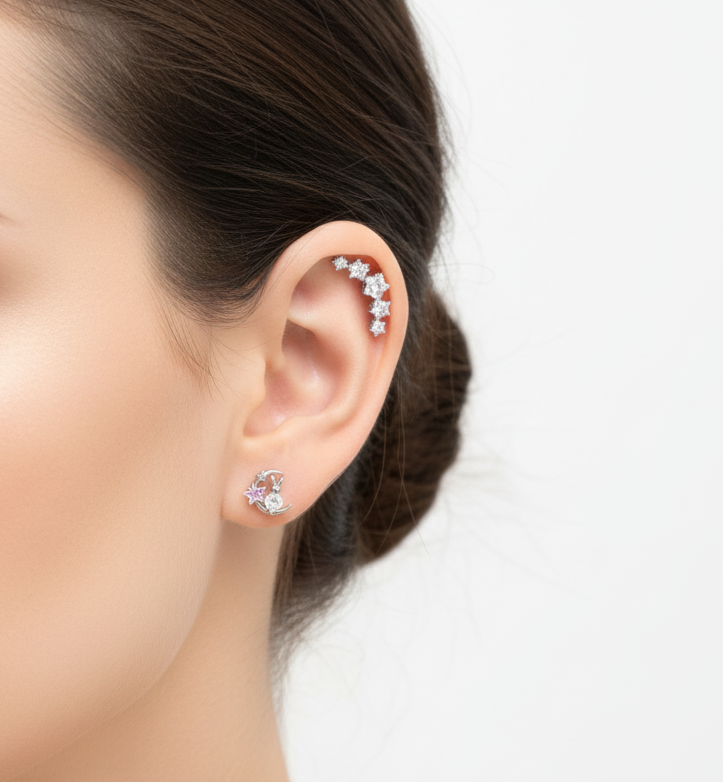 A woman’s ear styled with a moon and star cubic zirconia stud on the lobe and a constellation-like climber along the upper ear curve. Hair tied back in a neat bun.