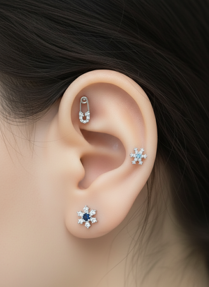 Layered ear styling with three earrings: snowflake studs in different sizes and a safety pin barbell in the inner cartilage.