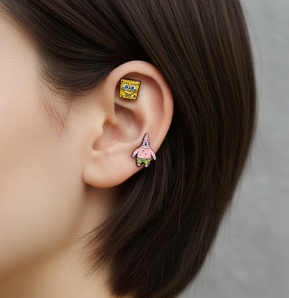 SpongeBob and Patrick enamel barbell earrings styled on a single ear — SpongeBob on the upper cartilage, Patrick on the lobe.