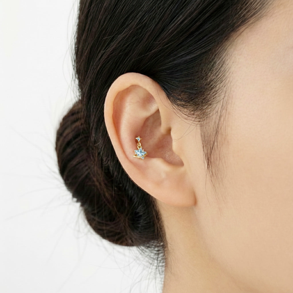 Model wearing a gold and blue cubic zirconia planet piercing in the inner conch area.