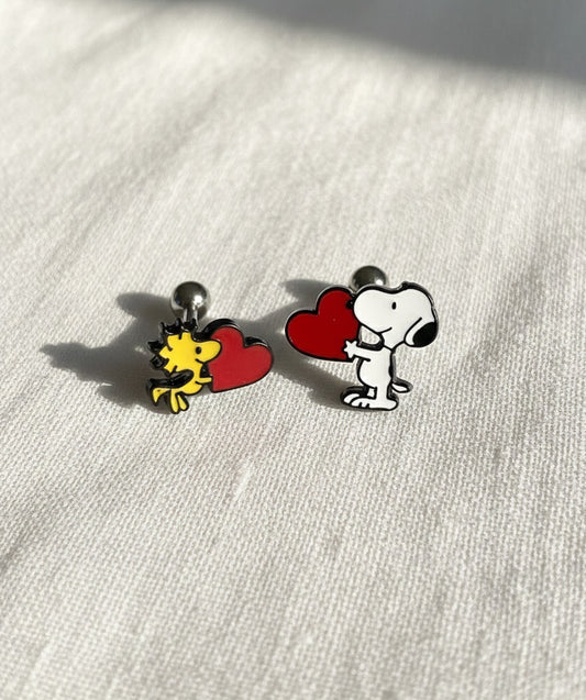 Snoopy and Woodstock heart earrings photographed under natural sunlight on soft fabric background.