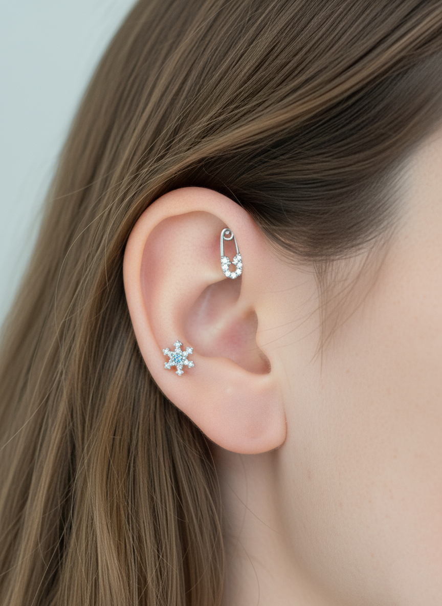Matching silver snowflake studs and barbell safety pin styled across upper and lower ear, worn with straight brown hair.