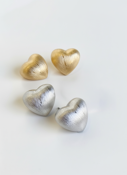 gold and silver brushed-metal heart studs arranged on a white surface, showing both colors together