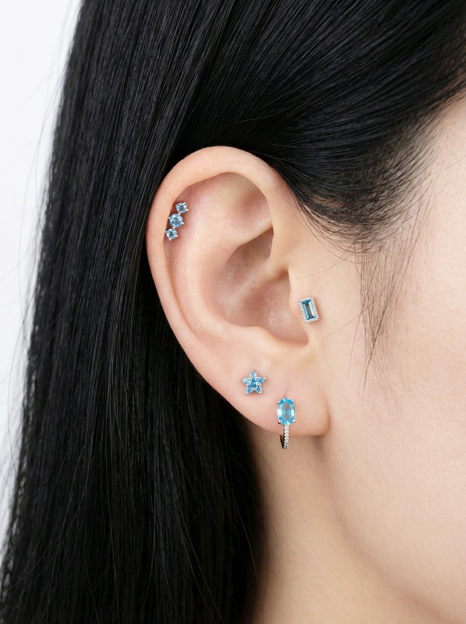 Ear styling with a rectangular blue CZ barbell combined with blue star, cluster, and hoop earrings.