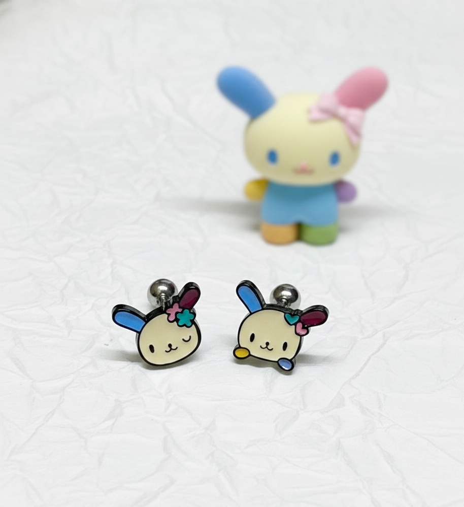 two Ussahana-inspired pastel bunny-face barbell studs displayed on textured white paper with a blurred bunny figurine in the background