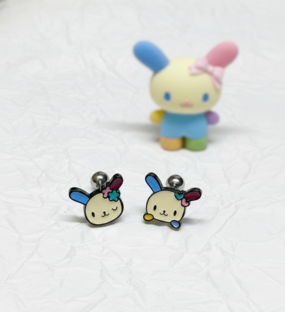 two Ussahana-inspired pastel bunny-face barbell studs displayed on textured white paper with a blurred bunny figurine in the background