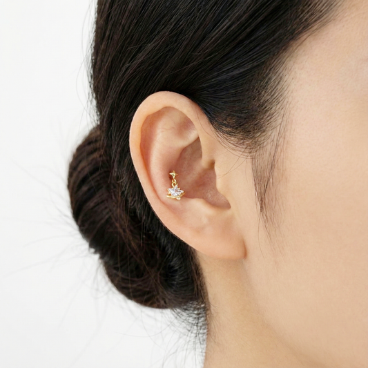 Close-up of a gold planet piercing with clear stone worn in the inner conch position.