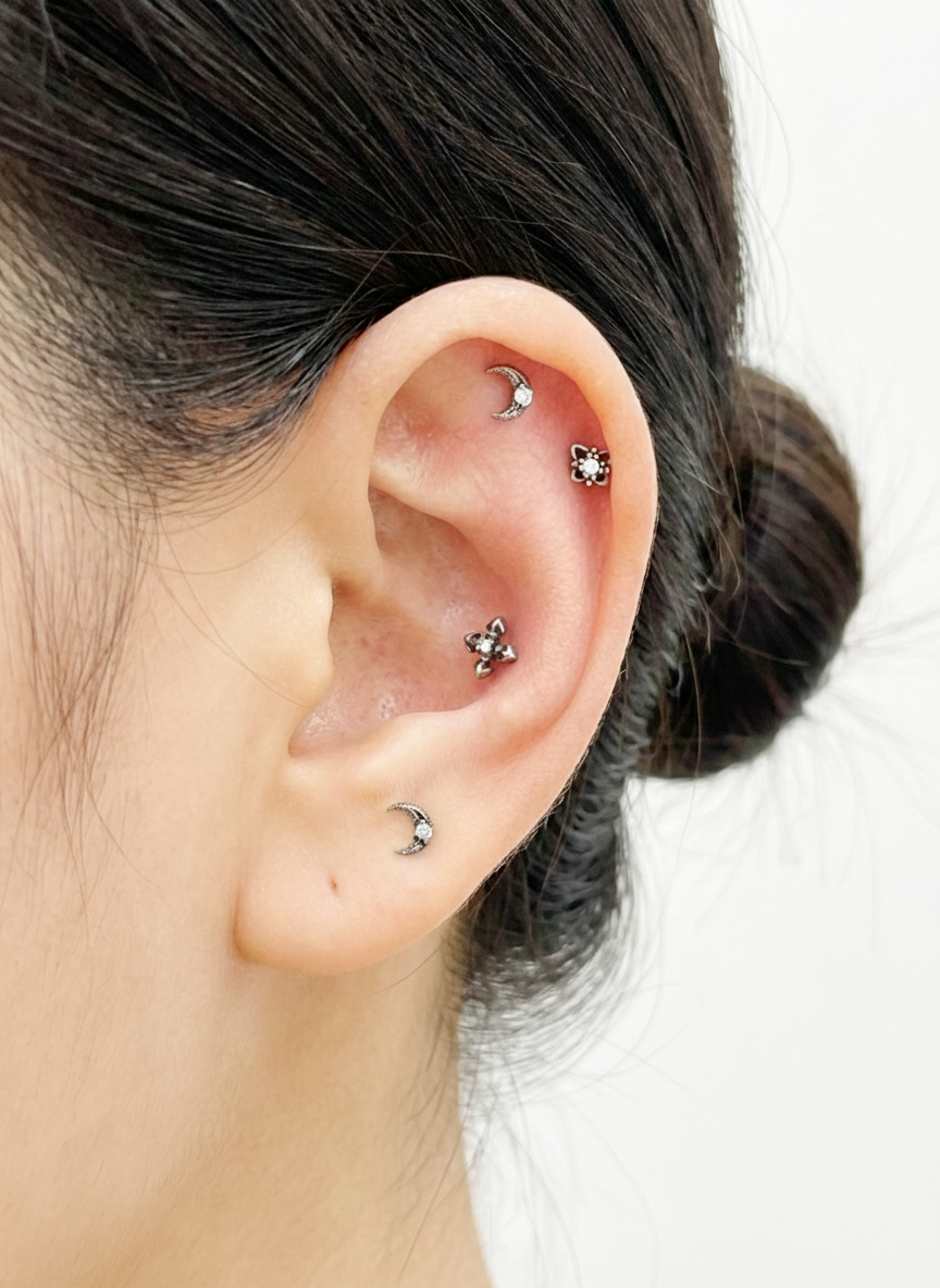 close-up ear photo showing moon, star, and cross gothic barbell studs in silver surgical steel on cartilage piercings