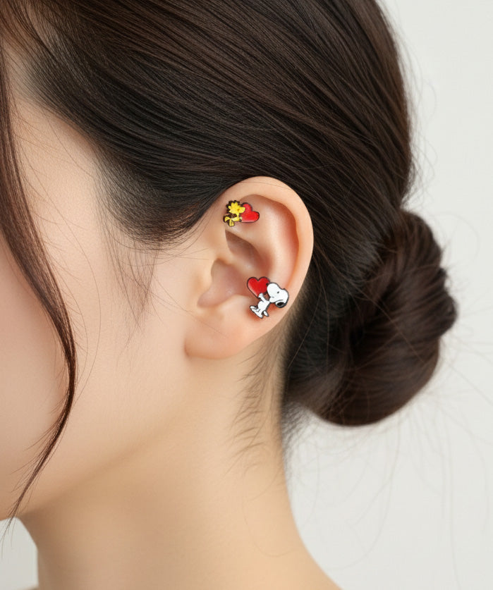 Snoopy and Woodstock heart earrings worn together on one ear – cartilage and lobe piercings visible.