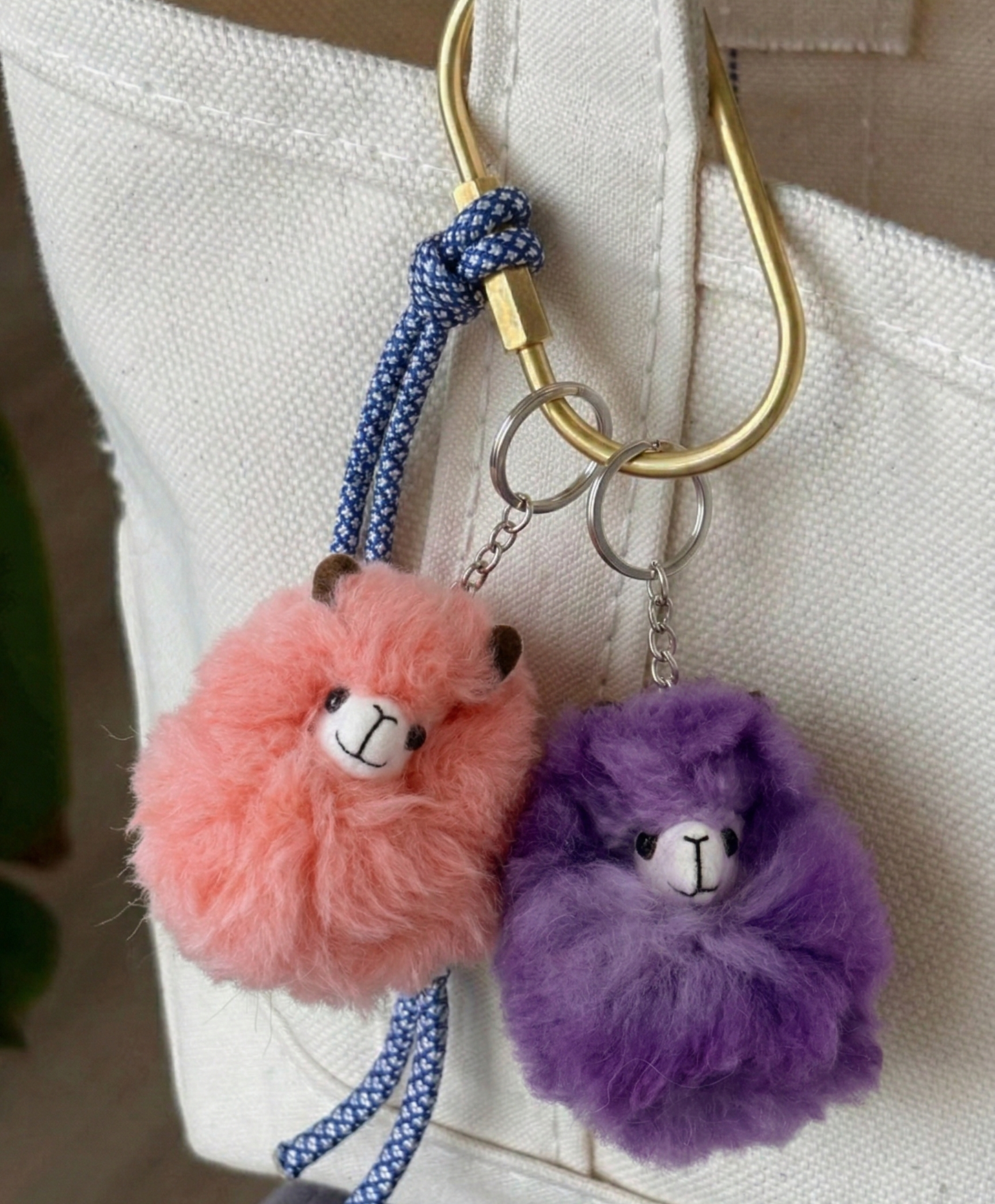 Two fluffy keychains, one pink and one purple, attached to a bag with a gold hook.
