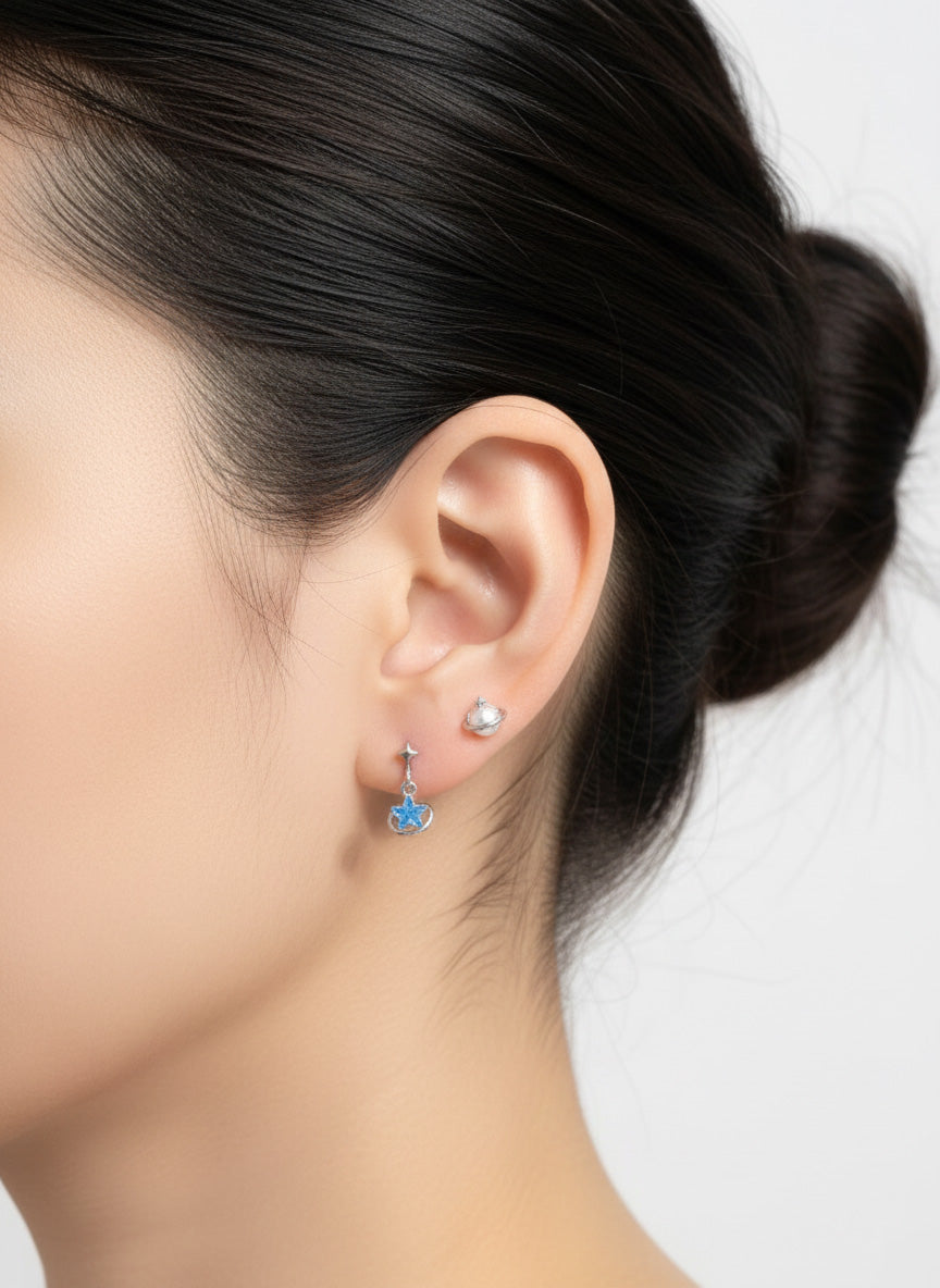Side profile showing a silver and blue star planet earring paired with a second silver stud on the lobe.