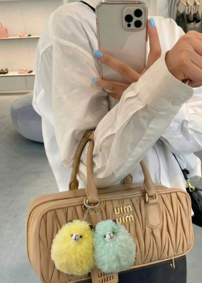 Person holding a beige handbag with fluffy keychains in a store setting