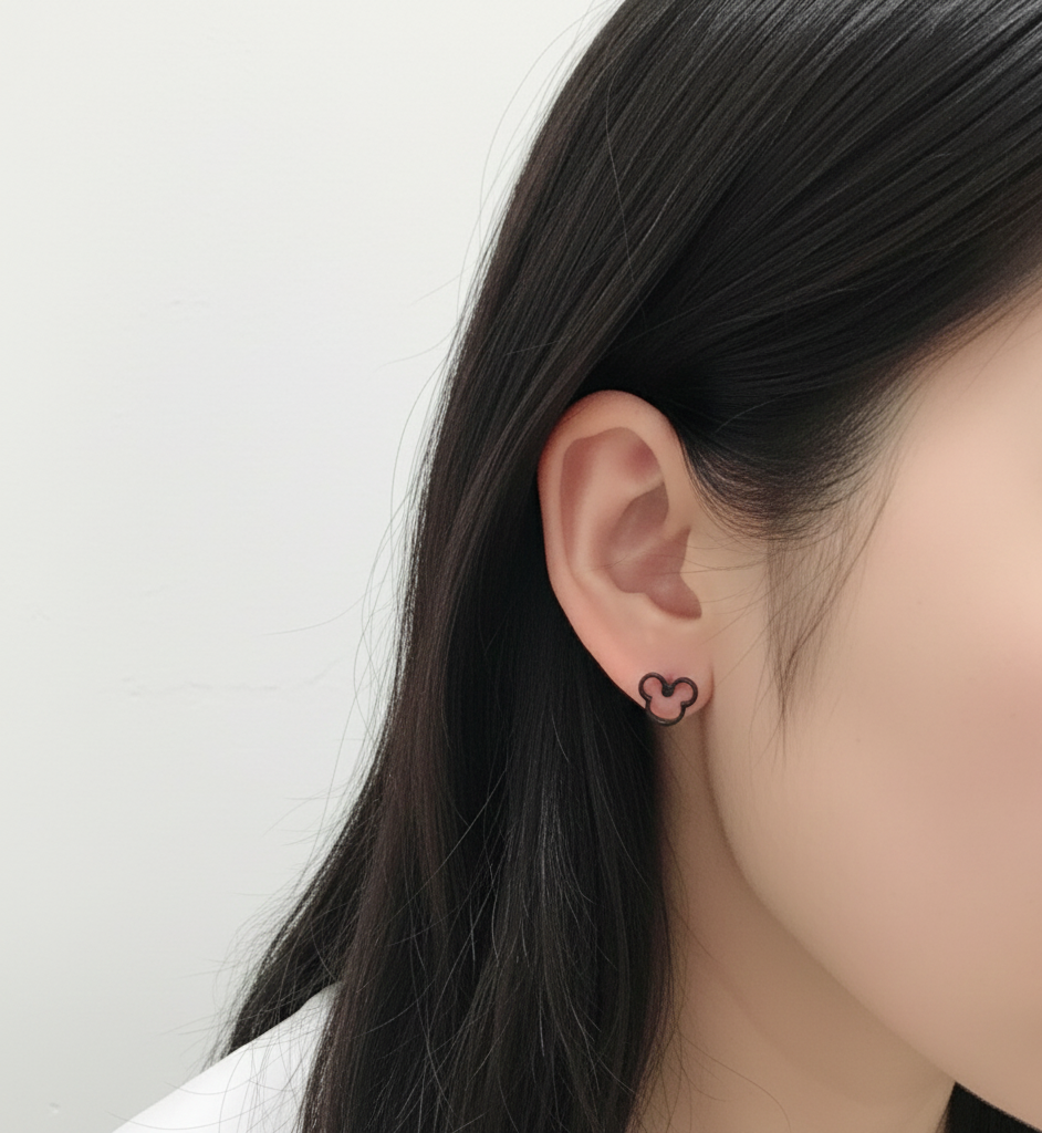 Side view of ear wearing a black Mickey head silhouette earring, styled with natural straight hair.