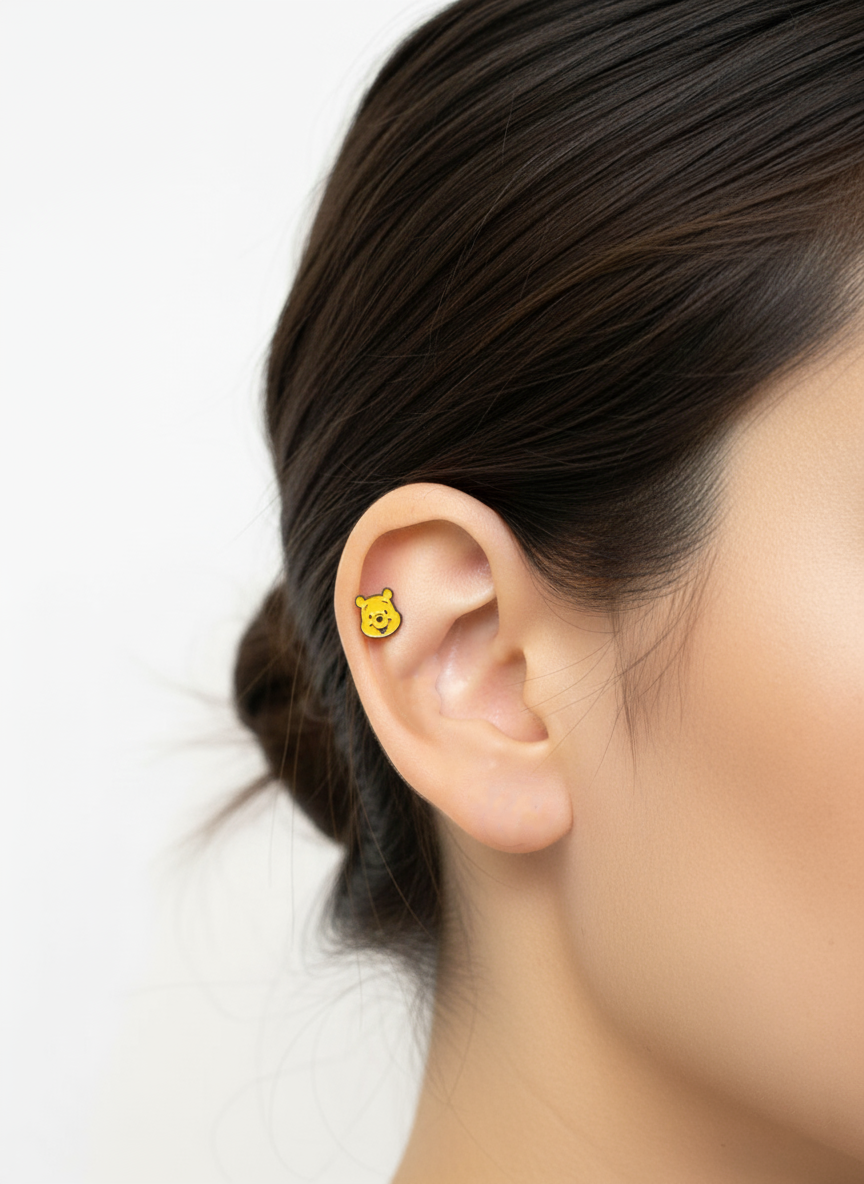 One Pooh character piercing worn on inner ear helix area against a soft white background.