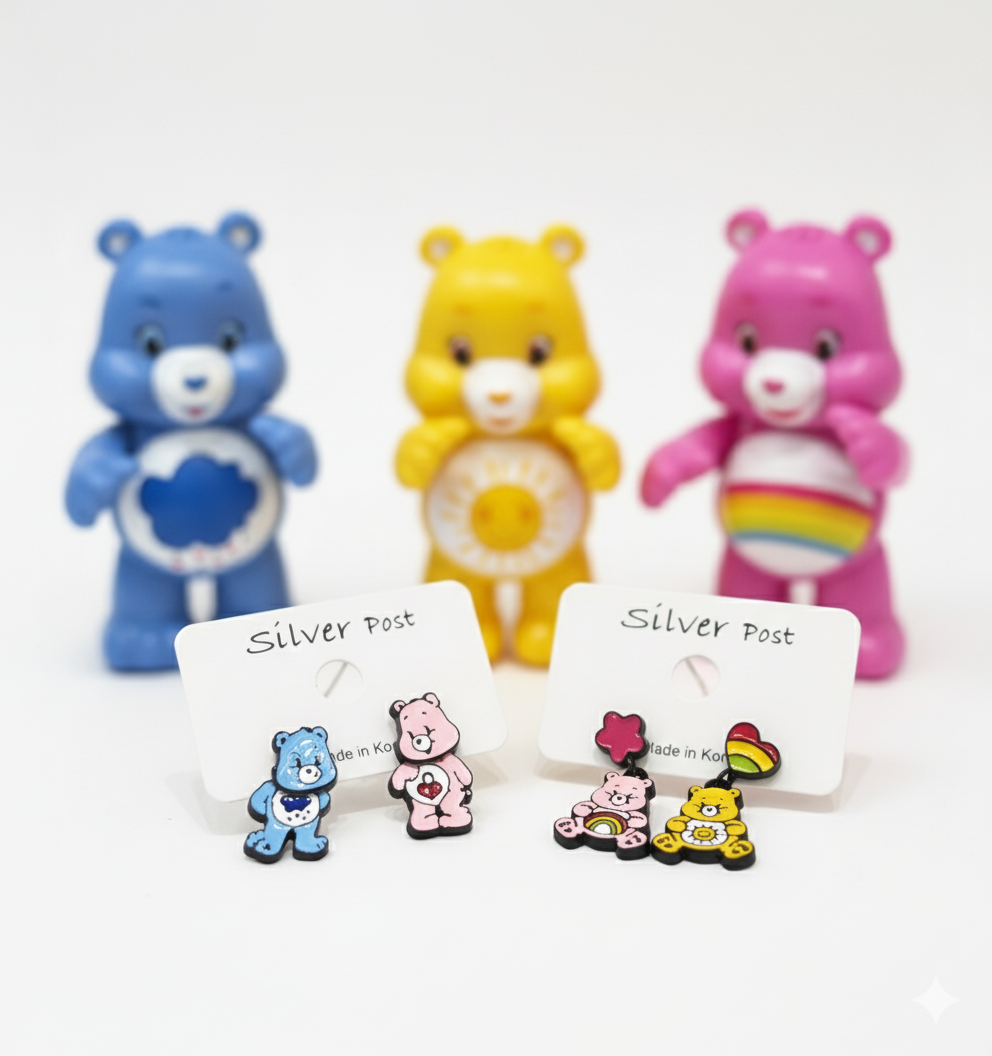 Two sets of colorful bear earrings displayed on white earring cards, with matching yellow, pink, and blue bear figurines blurred in the background.