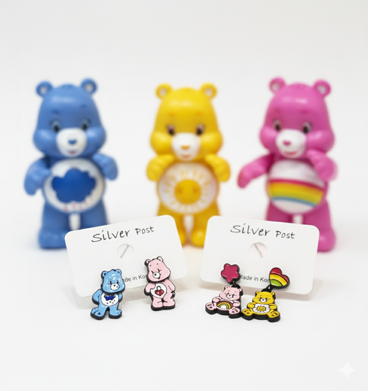 Two sets of colorful bear earrings displayed on white earring cards, with matching yellow, pink, and blue bear figurines blurred in the background.