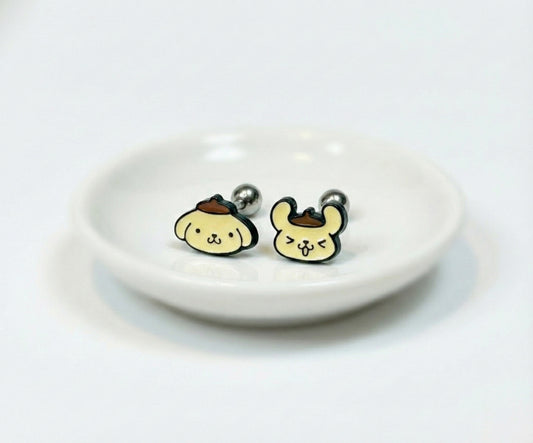 Two Pompompurin-themed barbell piercings with different facial expressions displayed in a round white dish.