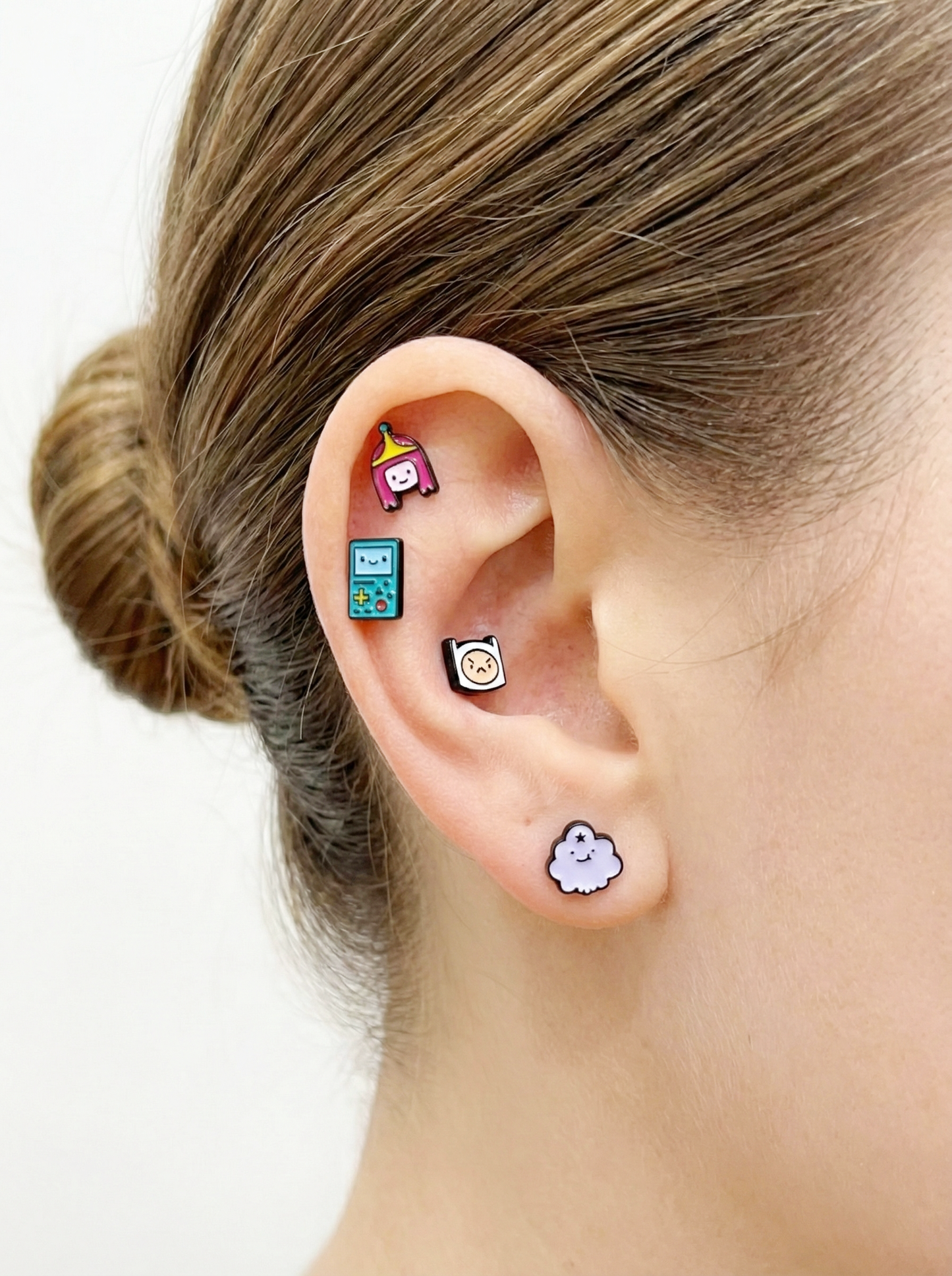 Full ear styling with four Adventure Time earrings: Princess Bubblegum on the helix, BMO and Finn in the middle, Lumpy Space Princess on the lobe.