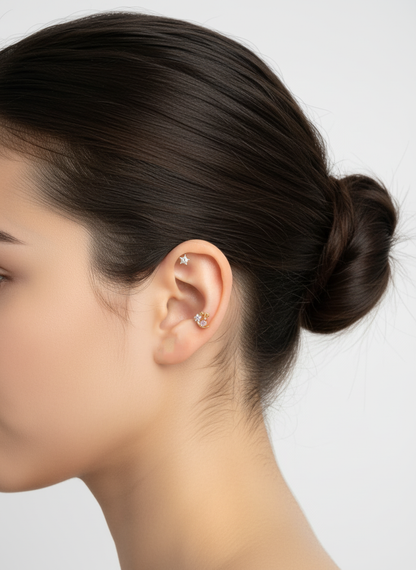Profile shot of a woman’s ear with a dainty gold moon and star earring on the helix and a white star stud on the upper lobe. Soft lighting and clean background.