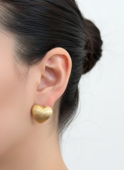 gold brushed-metal heart stud earring on the ear, highlighting the smooth matte finish and domed heart shape