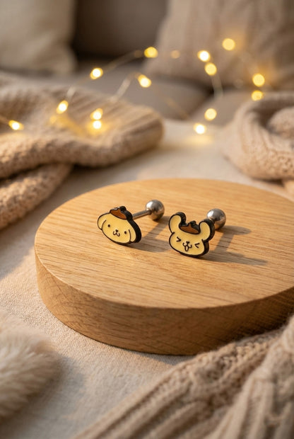 Cozy lifestyle shot of Pompompurin barbell piercings placed on a wooden display with warm lighting and knit textures in the background.