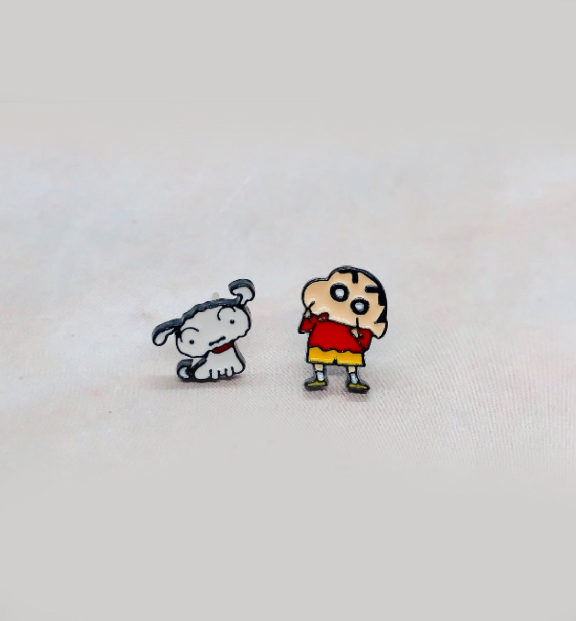 Crayon Shin-chan inspired white dog stud and child figure stud displayed on a soft fabric surface