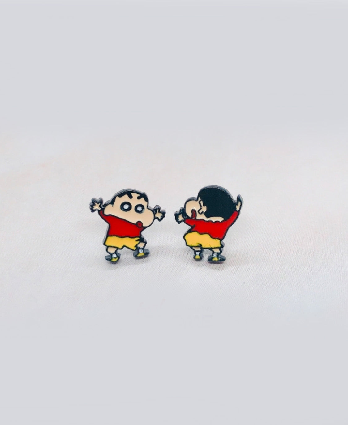 Crayon Shin-chan inspired child figure stud earrings in red tops and yellow shorts, shown on a fabric surface with front and back poses.