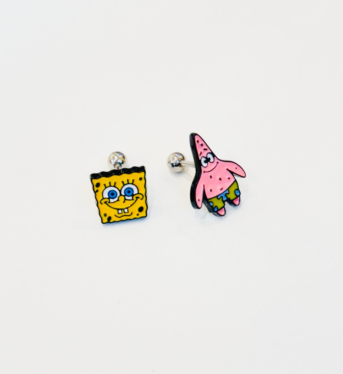 Matching pair of SpongeBob and Patrick enamel barbell earrings with stainless steel posts, laid on white surface