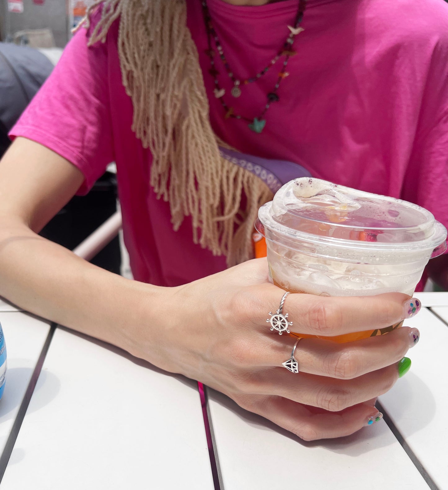Hand holding iced tea wearing silver steering wheel ring summer lifestyle