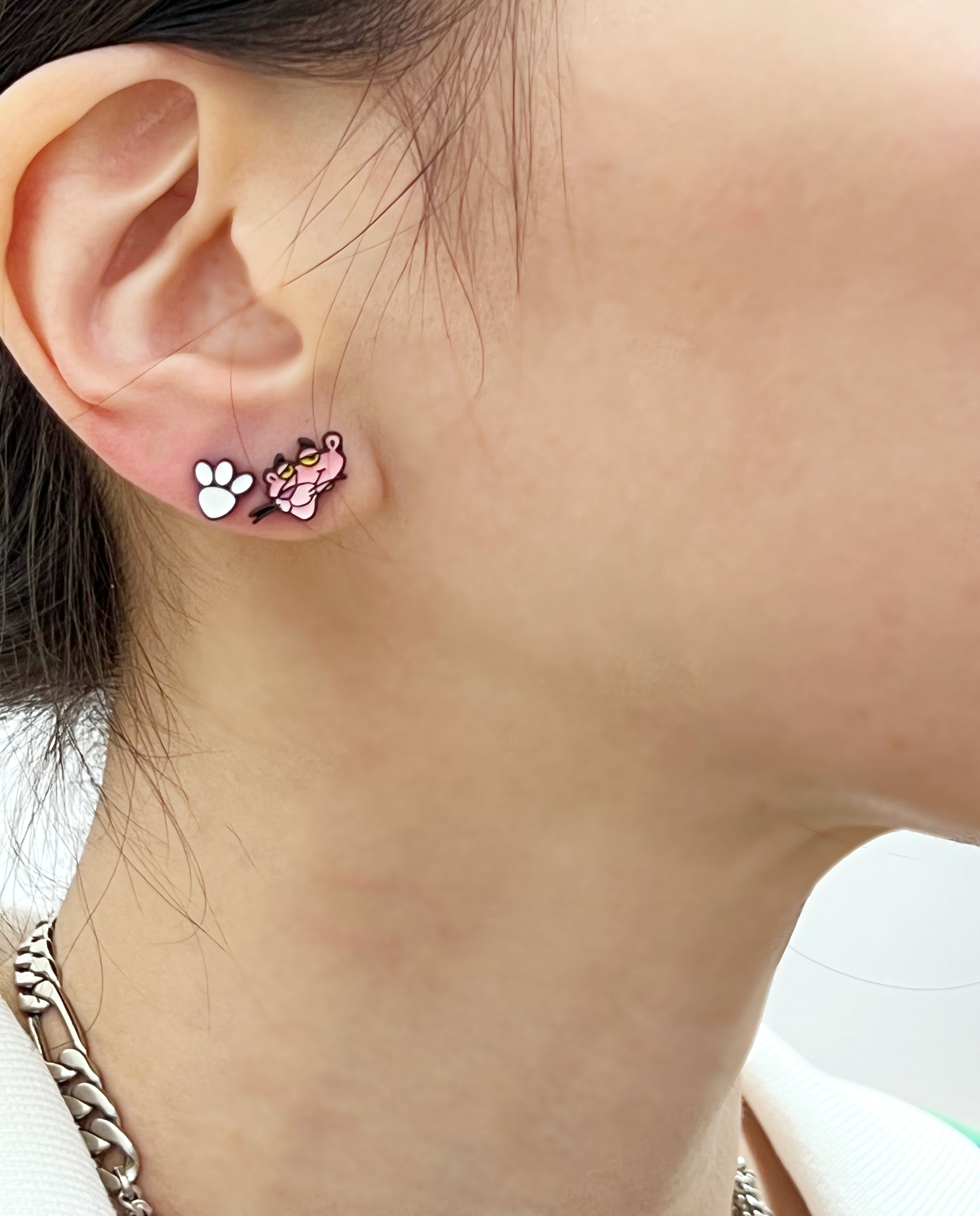 Model wearing Pink Panther head and white paw stud earrings, close-up on earlobe, styled with a silver chain necklace