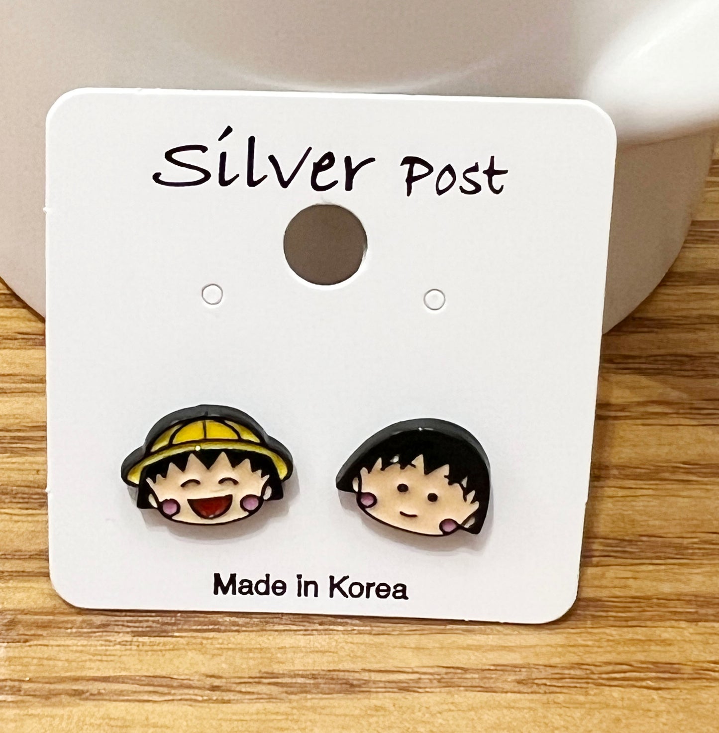 Front view of Chibi Maruko-chan enamel earrings showing yellow hat and bob haircut designs