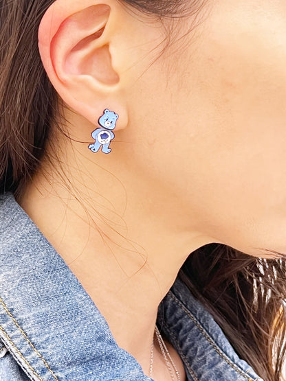 Blue bear character earring worn on a clean ear lobe, styled with a denim collar and soft daylight setting.