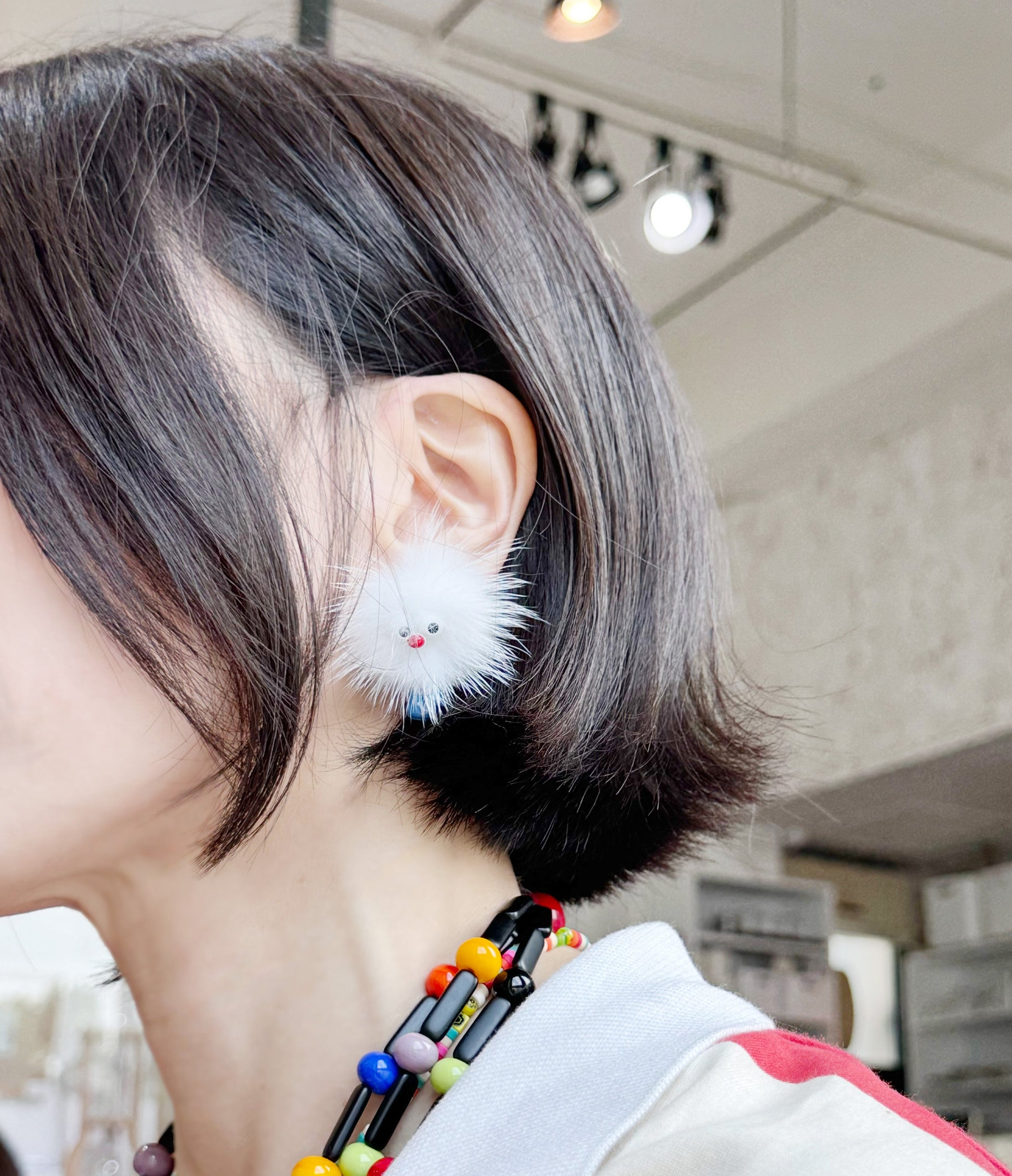 Person wearing a white fluffy character earring with blue feet, short bob hairstyle, indoor setting