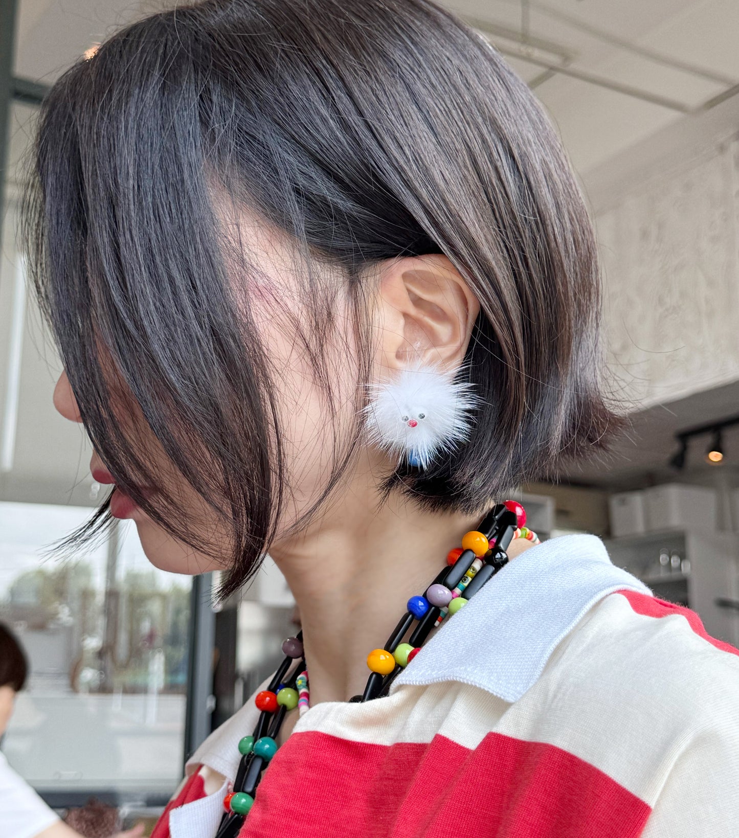 Side profile showing white fluffy earring with blue feet worn with a bob haircut