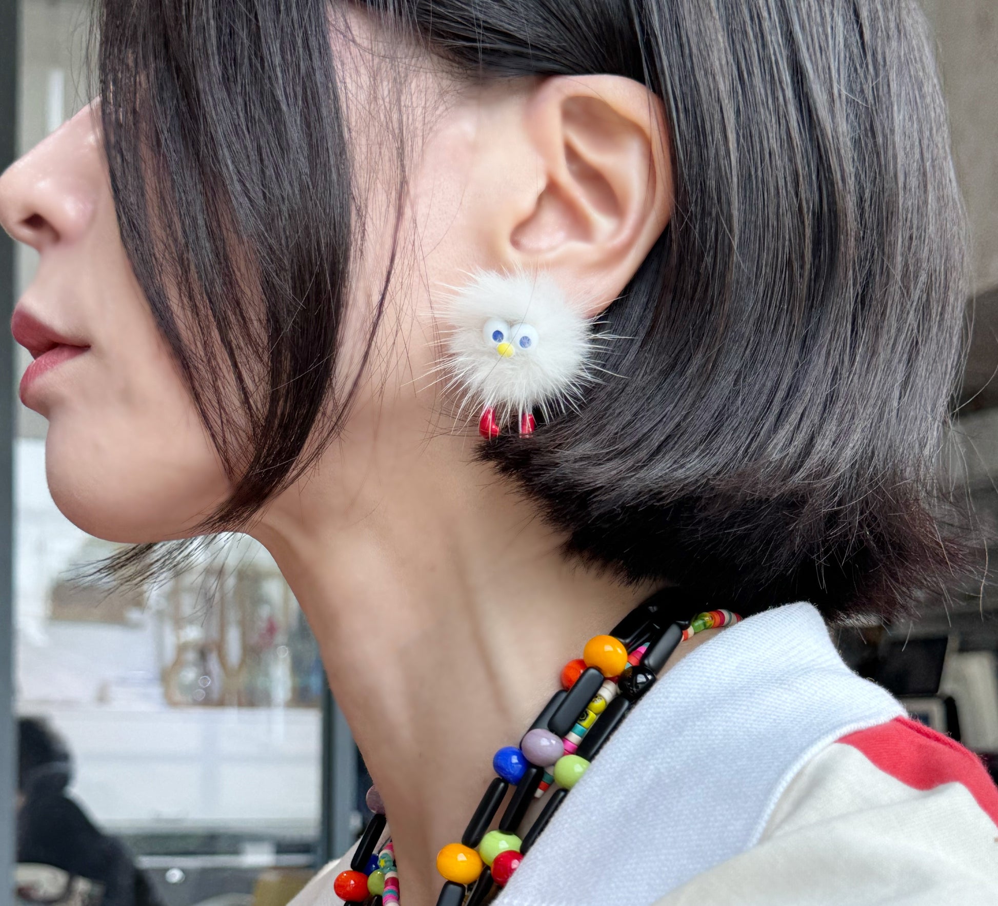 Close-up of a white fluffy earring with red feet on the ear, paired with a striped top.