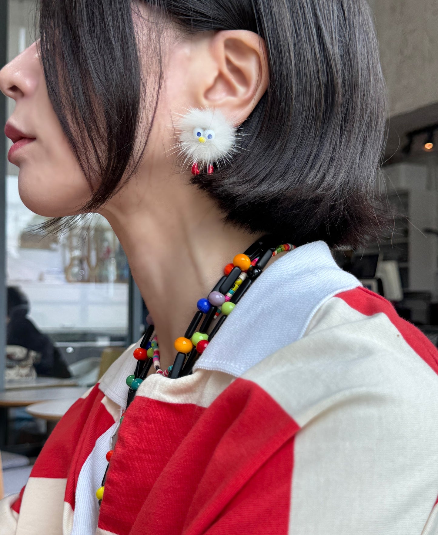 Side portrait showing a white fluffy character earring with red feet, short bob hairstyle.