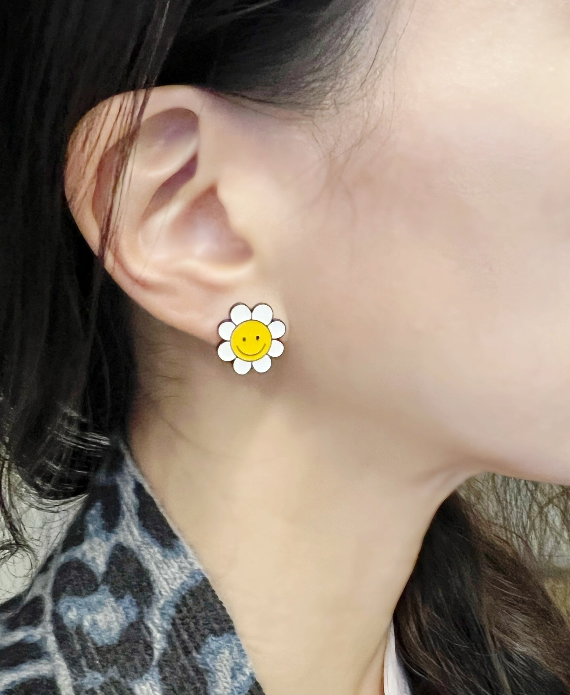 White petal smiley flower stud earring worn on the left ear, paired with a neutral-toned outfit and soft lighting.